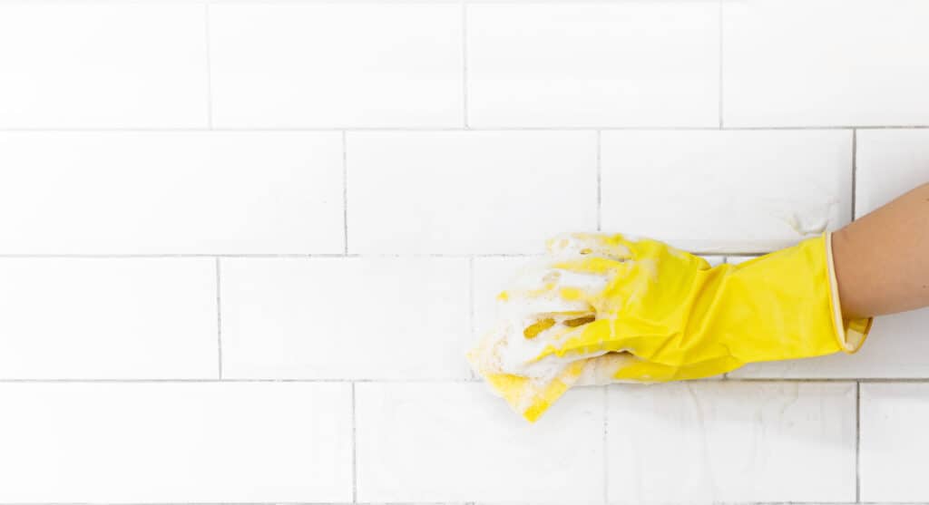 A female hand in a yellow latex glove sponges a tile. There is a lot of foam in the sink. The concept of cleaning the bathroom or kitchen, cleanliness. Copyspace for text